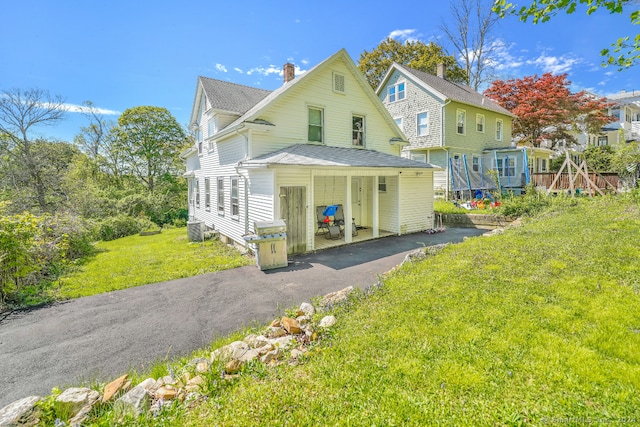 view of front of house with a shingled roof, aphalt driveway, a front yard, central AC unit, and a chimney