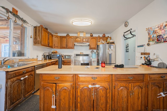 kitchen featuring brown cabinetry, a sink, light countertops, under cabinet range hood, and appliances with stainless steel finishes