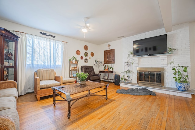 living area with beamed ceiling, a fireplace, a ceiling fan, and hardwood / wood-style floors
