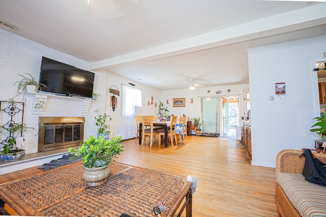 living room with light wood finished floors, visible vents, beamed ceiling, a fireplace, and a ceiling fan