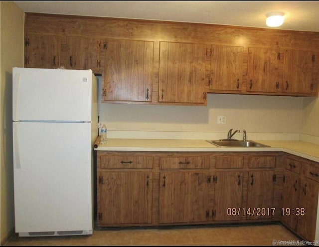 kitchen featuring freestanding refrigerator, brown cabinets, a sink, and light countertops