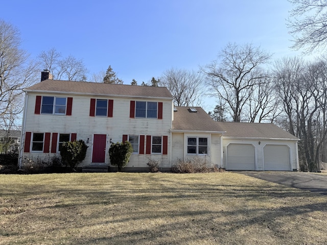 colonial-style house featuring aphalt driveway, entry steps, a front yard, a chimney, and an attached garage