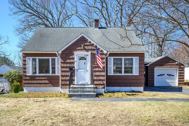 bungalow-style home with a front lawn, entry steps, a detached garage, a shingled roof, and a chimney