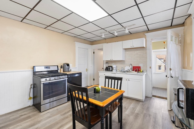 kitchen featuring white cabinetry, stainless steel range with gas stovetop, a drop ceiling, a sink, and dishwasher