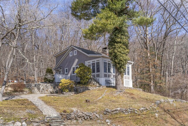 view of front of home featuring a chimney, a sunroom, and a view of trees