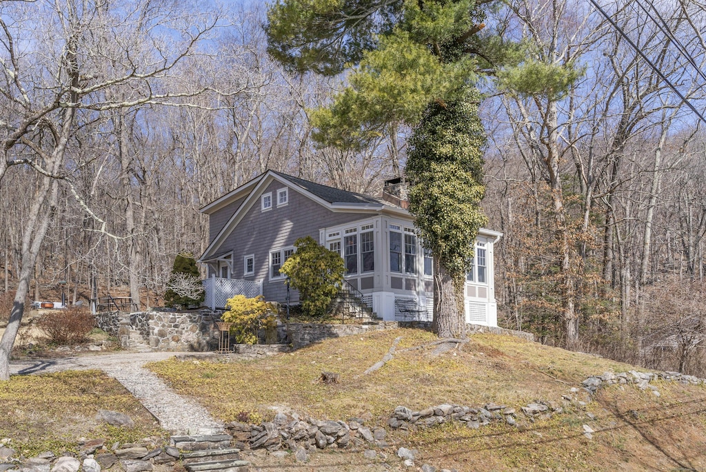 view of front of property featuring a wooded view, a sunroom, and a chimney