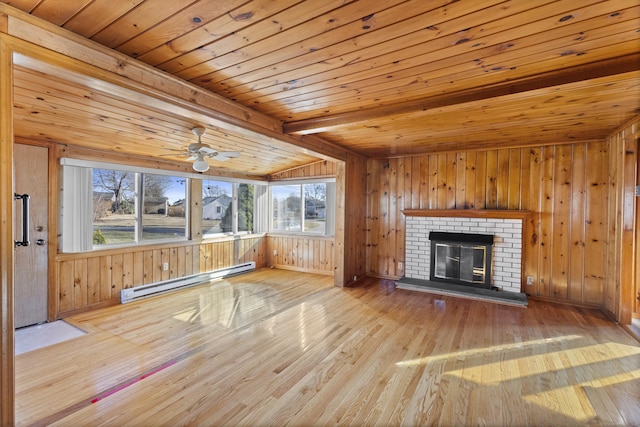unfurnished living room with a ceiling fan, a baseboard heating unit, wood finished floors, wooden walls, and a fireplace