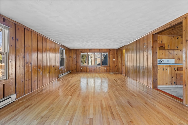 unfurnished living room with a baseboard heating unit, a healthy amount of sunlight, and light wood-style flooring