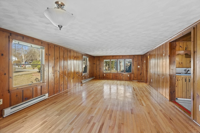 unfurnished living room featuring wood walls, light wood-type flooring, baseboard heating, and a sink