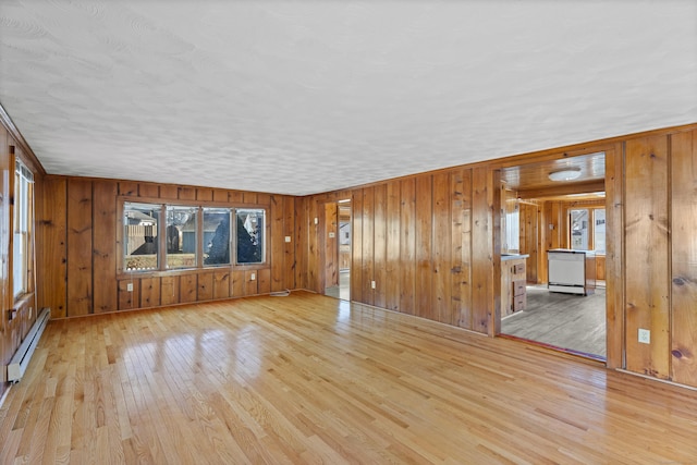 unfurnished living room featuring wooden walls, hardwood / wood-style flooring, and a baseboard radiator