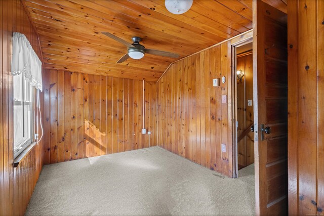 carpeted spare room with wood ceiling, wood walls, and a ceiling fan
