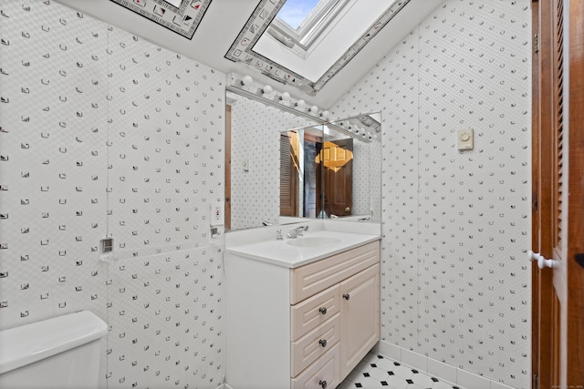 bathroom featuring wallpapered walls, lofted ceiling with skylight, toilet, and vanity