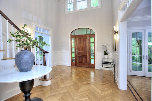 foyer entrance with a high ceiling, a decorative wall, stairs, wainscoting, and french doors