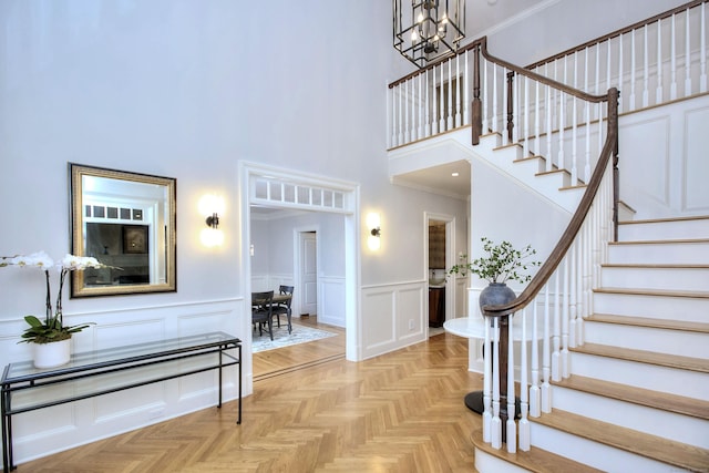 entrance foyer with a decorative wall, a chandelier, stairs, a towering ceiling, and a wainscoted wall