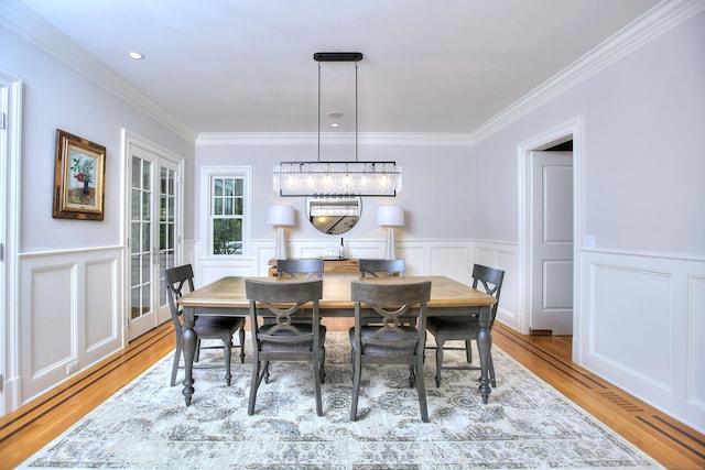 dining space with ornamental molding, wood finished floors, a decorative wall, and a wainscoted wall
