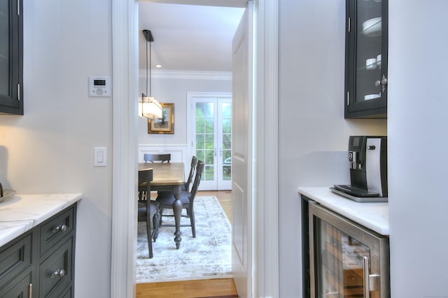 indoor dry bar with beverage cooler, ornamental molding, and light wood-style floors
