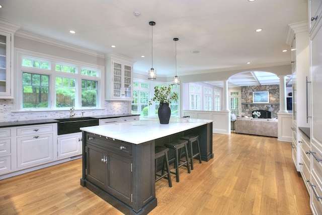 kitchen featuring a sink, decorative columns, white cabinets, a breakfast bar, and light wood-style floors