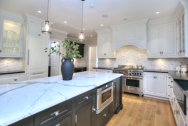 kitchen with stainless steel appliances, white cabinetry, pendant lighting, glass insert cabinets, and dark stone counters