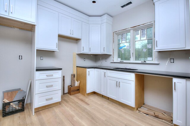 kitchen with light wood-style floors, white cabinetry, dark countertops, and built in desk