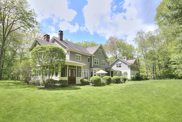 back of house with a yard, a chimney, a sunroom, and a shingled roof