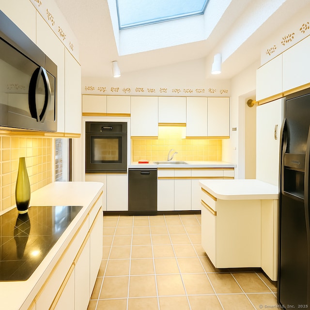 kitchen featuring tasteful backsplash, a skylight, light countertops, black appliances, and a sink