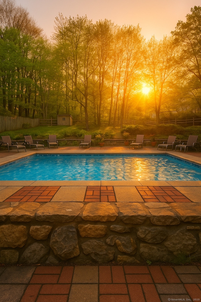 pool at dusk with an outdoor structure, a shed, fence, and a patio area