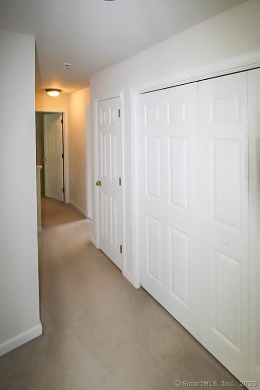 hall featuring baseboards and light carpet