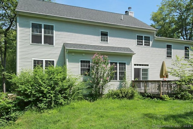 back of property featuring a deck, a lawn, and a chimney