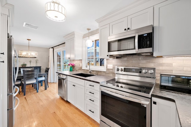 12 Nevins Ave, Enfield, CT 06082 - kitchen featuring appliances with stainless steel finishes, backsplash, light wood finished floors, white cabinetry, and pendant lighting