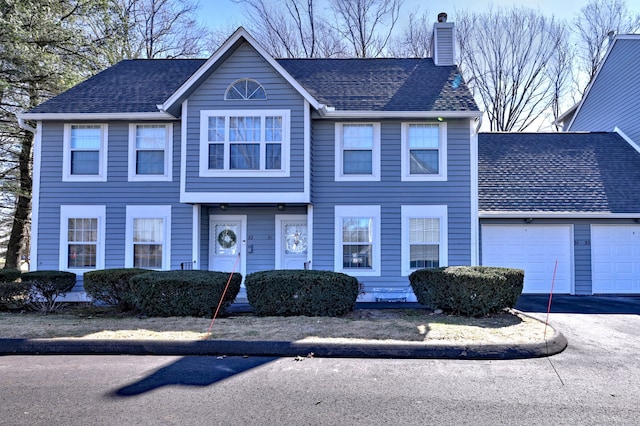 view of front of home with an attached garage, a chimney, and driveway