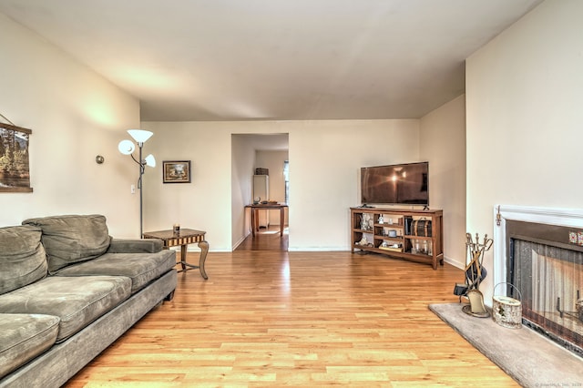 living area featuring baseboards, light wood-style flooring, and a fireplace with raised hearth