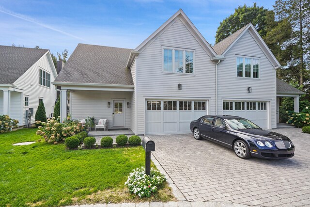 view of front of house featuring an attached garage, decorative driveway, a front yard, and roof with shingles