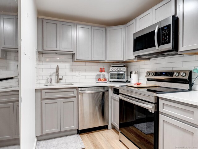 kitchen featuring gray cabinetry, a sink, stainless steel appliances, light countertops, and decorative backsplash