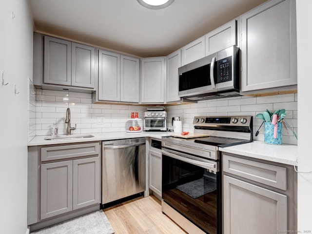kitchen featuring light wood finished floors, gray cabinetry, appliances with stainless steel finishes, and a sink