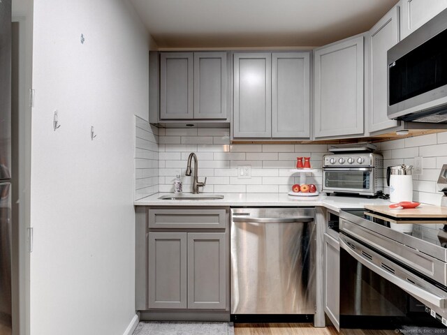 kitchen with gray cabinetry, stainless steel appliances, light countertops, and a sink