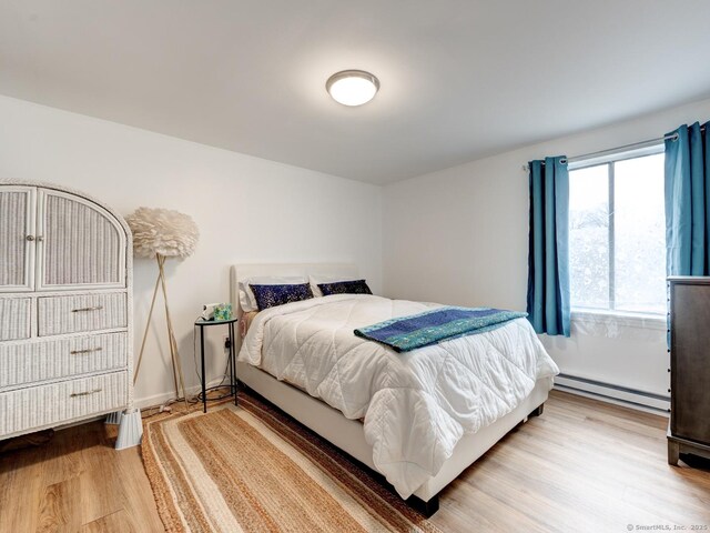 bedroom featuring baseboards, light wood-type flooring, and a baseboard radiator