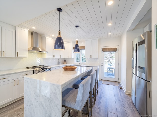 kitchen with tasteful backsplash, appliances with stainless steel finishes, wall chimney exhaust hood, and wood finished floors