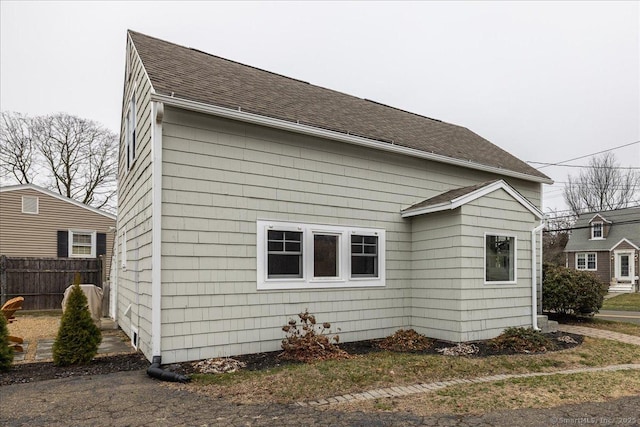 view of home's exterior featuring roof with shingles and fence