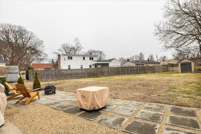 view of yard with a shed, an outdoor fire pit, a fenced backyard, an outbuilding, and a patio