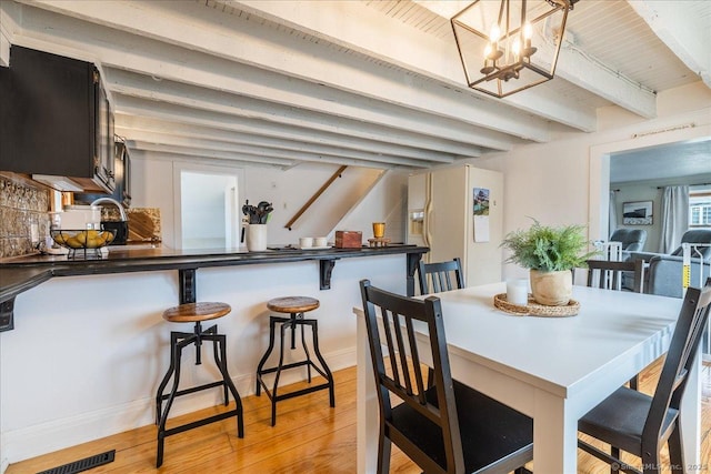 dining area with beam ceiling, visible vents, light wood-type flooring, and a chandelier
