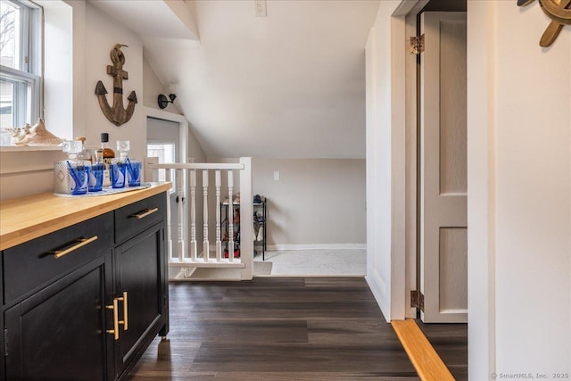 corridor featuring dark wood-style floors, baseboards, and lofted ceiling