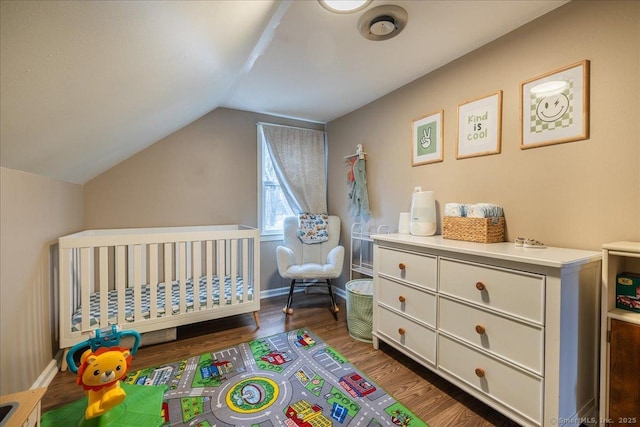 bedroom featuring a crib, lofted ceiling, wood finished floors, and baseboards