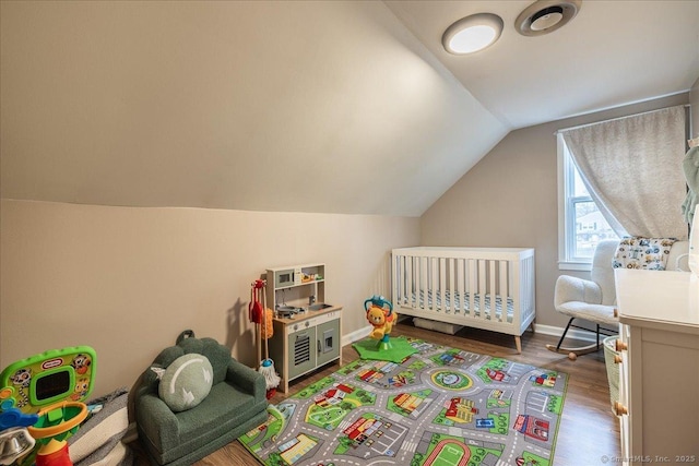bedroom with a nursery area, baseboards, lofted ceiling, and wood finished floors