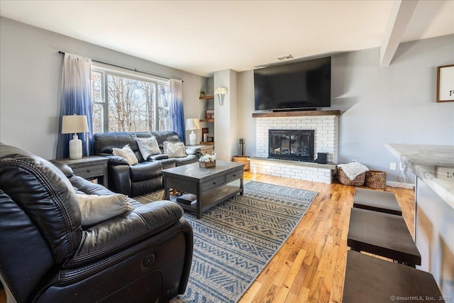 living room featuring a brick fireplace, baseboards, beamed ceiling, and wood finished floors