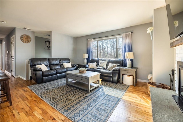 living room featuring hardwood / wood-style floors, baseboards, visible vents, and a glass covered fireplace