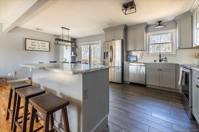 kitchen featuring dark wood finished floors, gray cabinets, tasteful backsplash, and appliances with stainless steel finishes