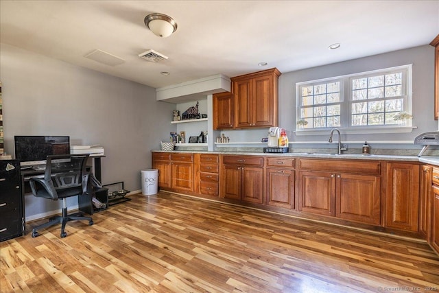 kitchen with light wood-type flooring, visible vents, a sink, and brown cabinets