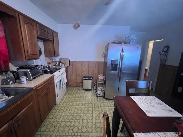 12 Avery St, Stonington, CT 06379 - kitchen with stainless steel refrigerator with ice dispenser, white electric range oven, wainscoting, light floors, and wooden walls