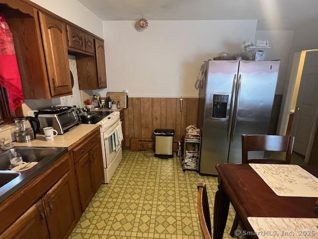 12 Avery St, Stonington, CT 06379 - kitchen with stainless steel refrigerator with ice dispenser, electric range, wainscoting, light floors, and wooden walls