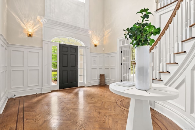 entryway with a decorative wall, a towering ceiling, stairs, and wainscoting
